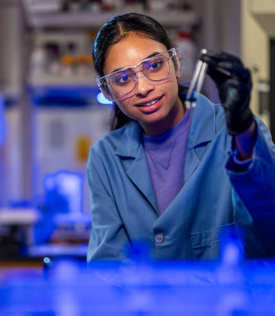 Two students wearing safety goggles and lab coats working together in a lab